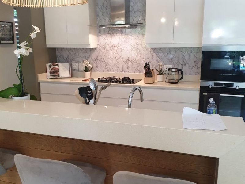 Modern kitchen featuring high-gloss cabinetry, marble-look splashback, quartz countertops, and a functional breakfast bar with integrated gas hob and built-in oven.