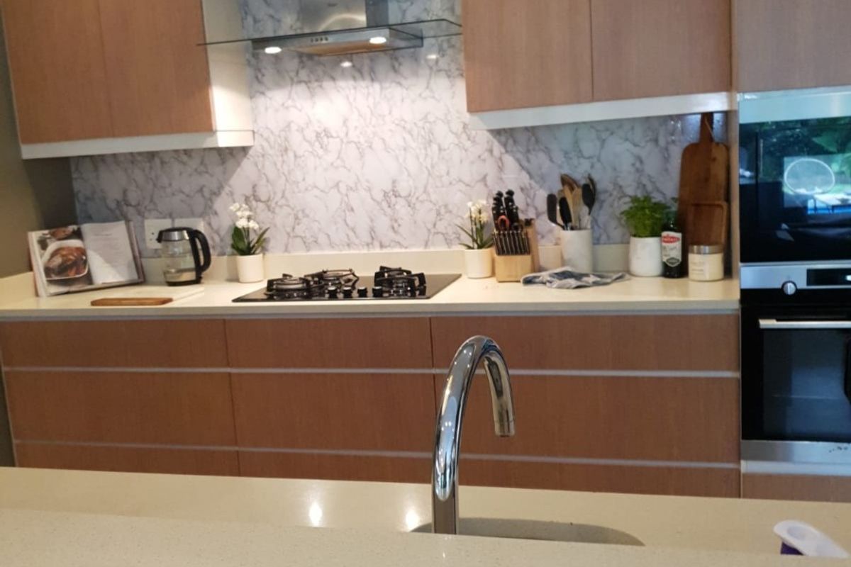 Modern kitchen featuring light wood cabinetry, stone countertops, marble-look splashback, gas hob, stainless steel extractor fan, and a built-in oven.
