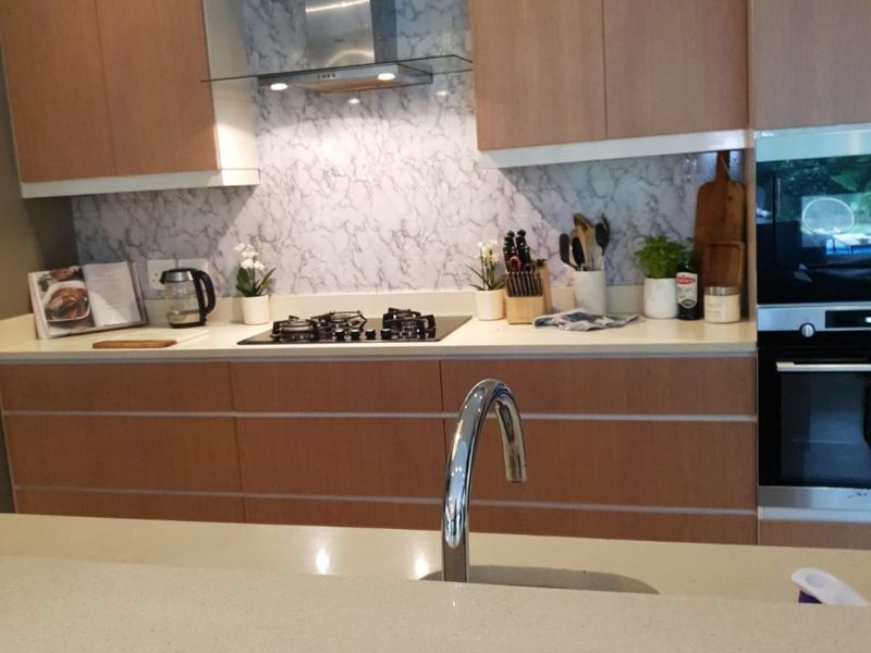 Modern kitchen featuring light wood cabinetry, stone countertops, marble-look splashback, gas hob, stainless steel extractor fan, and a built-in oven.