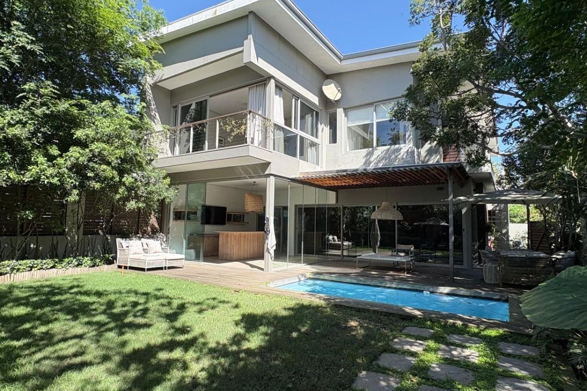 Rear view of a modern townhouse featuring a swimming pool, wooden decking, covered patio, and an upper-level balcony overlooking a landscaped garden.