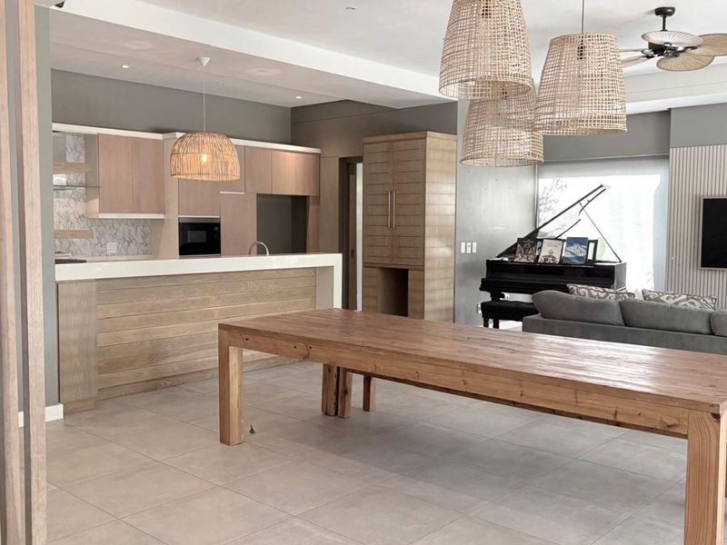 Spacious open-plan living and kitchen area featuring modern light wood cabinetry, stone countertops, tiled flooring, and contemporary pendant lighting.