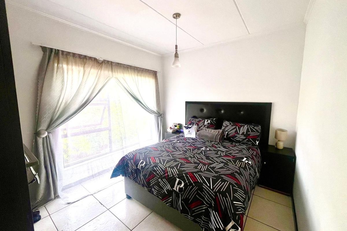 A bedroom featuring tiled flooring, a large window with natural light, and a ceiling pendant light fixture.