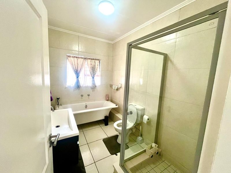 A functional bathroom featuring a freestanding bathtub, a separate glass-enclosed shower, a pedestal washbasin, and neutral ceramic tiling throughout.