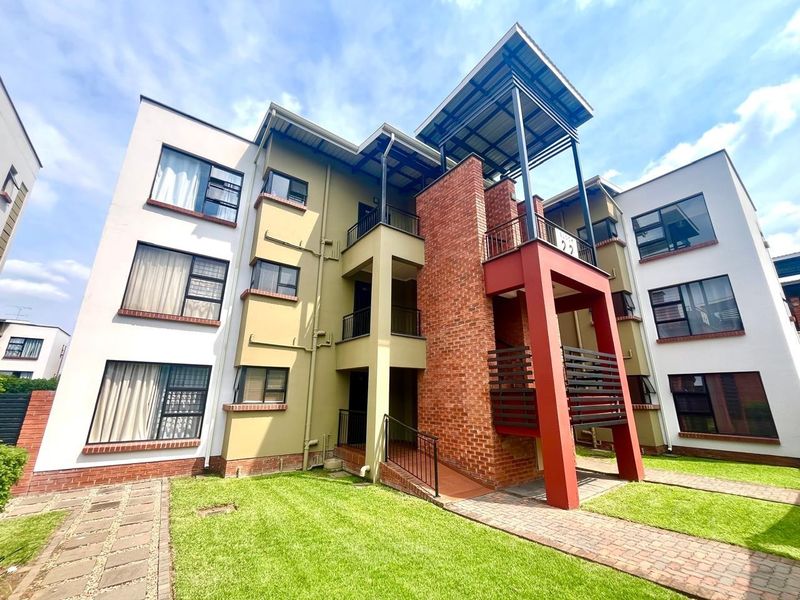 A well-maintained modern apartment building exterior featuring a mix of brick and rendered finishes, metal roofing, and landscaped grounds.