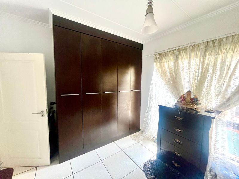 A bedroom featuring dark wood built-in cupboards, tiled flooring, and natural light through a window with curtains.
