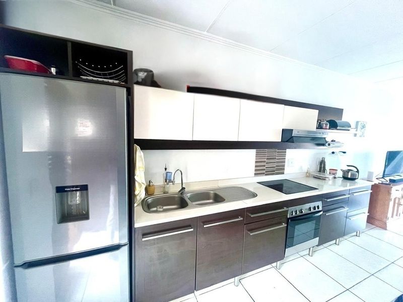 A functional kitchen featuring dark wood-finish cabinetry, contrasting white upper cabinets, integrated appliances including an oven and hob, and tiled flooring.