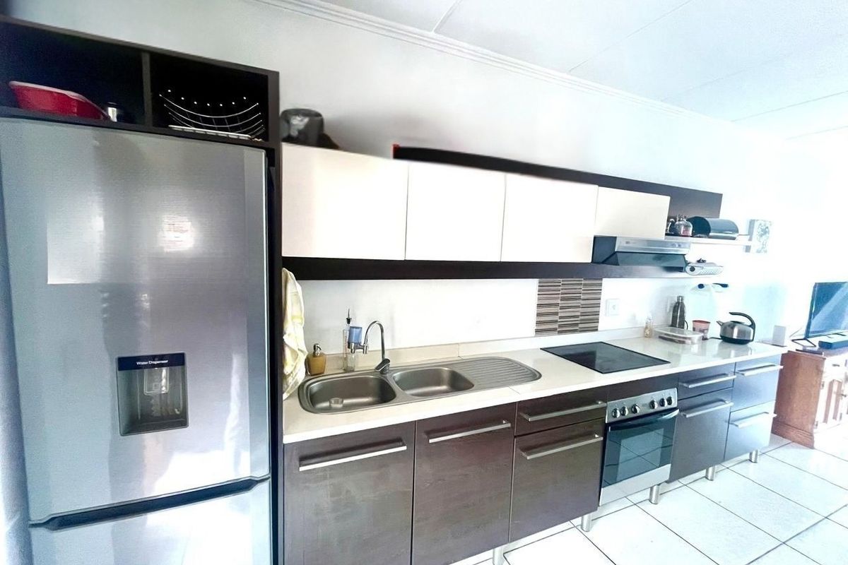 A functional kitchen featuring dark wood-finish cabinetry, contrasting white upper cabinets, integrated appliances including an oven and hob, and tiled flooring.