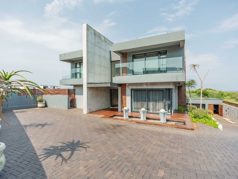 Modern architectural residence featuring a striking concrete facade, glass balustrades, paved driveway, and a contemporary water feature at the entrance.