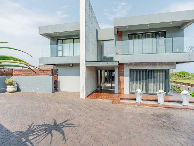 Modern architectural front elevation featuring concrete and timber finishes, glass balconies, and a paved driveway with an integrated water feature.