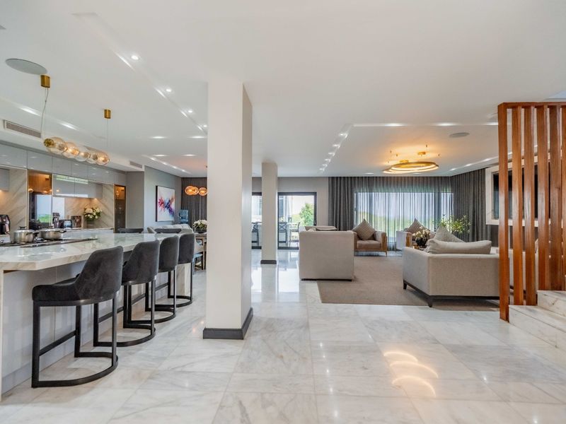 Spacious open-plan living area featuring high-end marble flooring, a modern kitchen island, and elegant wooden architectural accents, creating a seamless flow between spaces.