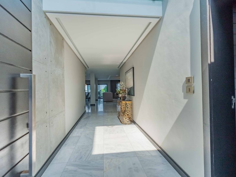 A modern, bright entrance hallway featuring polished marble flooring, a striking concrete feature wall, and a sleek recessed ceiling design leading into the home.