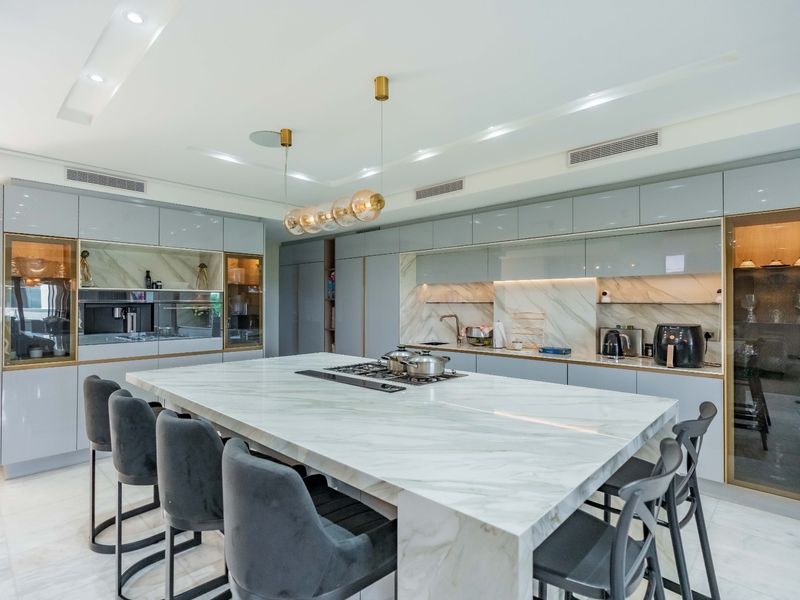 Modern luxury kitchen featuring a large marble island with integrated gas cooktop, sleek high-gloss cabinetry, and premium built-in appliances.