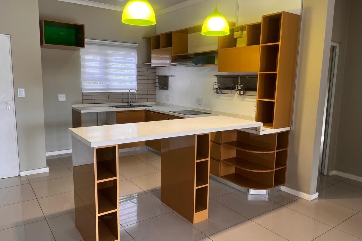 Modern kitchen featuring sleek cabinetry, a functional breakfast bar, stone countertops, integrated hob, and extractor fan, finished with neutral tiled flooring and backsplash.