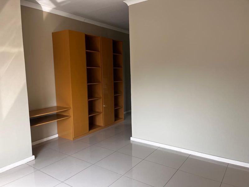 A bright, empty bedroom featuring neutral wall tones, modern tiled flooring, and extensive built-in storage cabinetry.