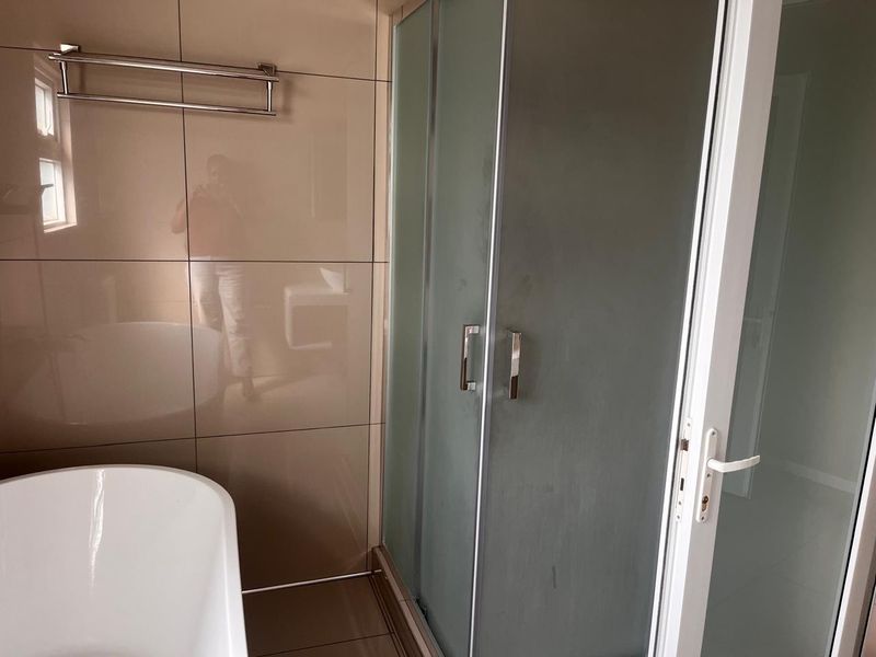A modern bathroom featuring a freestanding bathtub, a separate shower enclosure with frosted glass doors, and neutral wall tiling.
