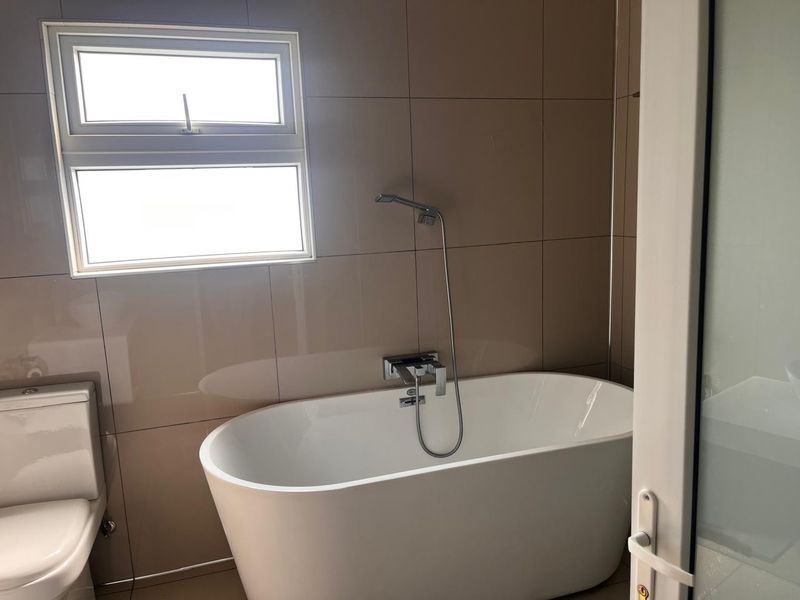 Modern bathroom featuring a sleek freestanding bathtub, wall-mounted shower mixer, and neutral tiled walls, providing a clean and contemporary aesthetic.