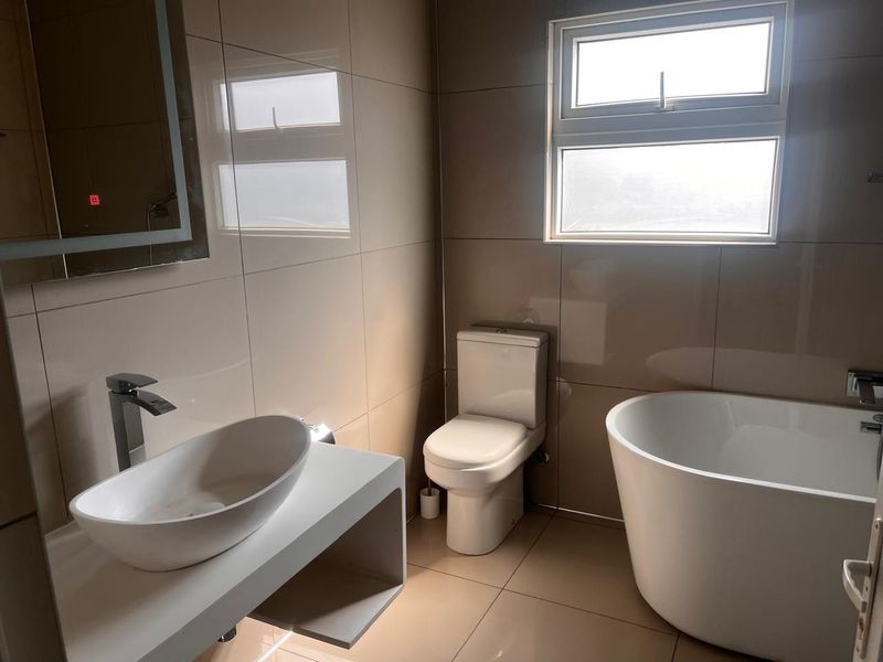 Modern bathroom featuring a sleek freestanding bathtub, vessel sink on a floating vanity, and contemporary tiled finishes with an integrated LED mirror.