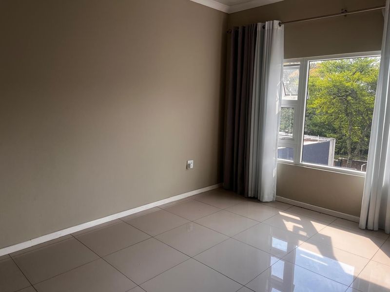 A bright and spacious bedroom featuring neutral wall tones, large windows with natural light, and clean tiled flooring throughout.