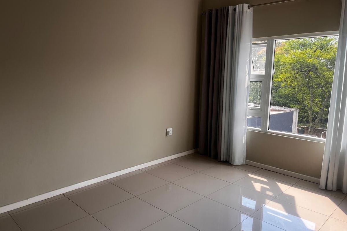 A bright and spacious bedroom featuring neutral wall tones, large windows with natural light, and clean tiled flooring throughout.