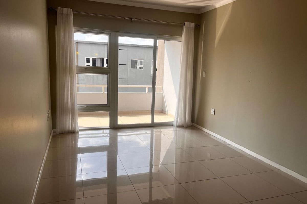 An empty living room featuring polished tile flooring, neutral wall tones, and a sliding glass door providing access to a private balcony.