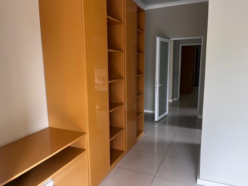 A bright hallway featuring extensive built-in storage cabinetry and polished floor tiles, leading through to additional rooms within the apartment.