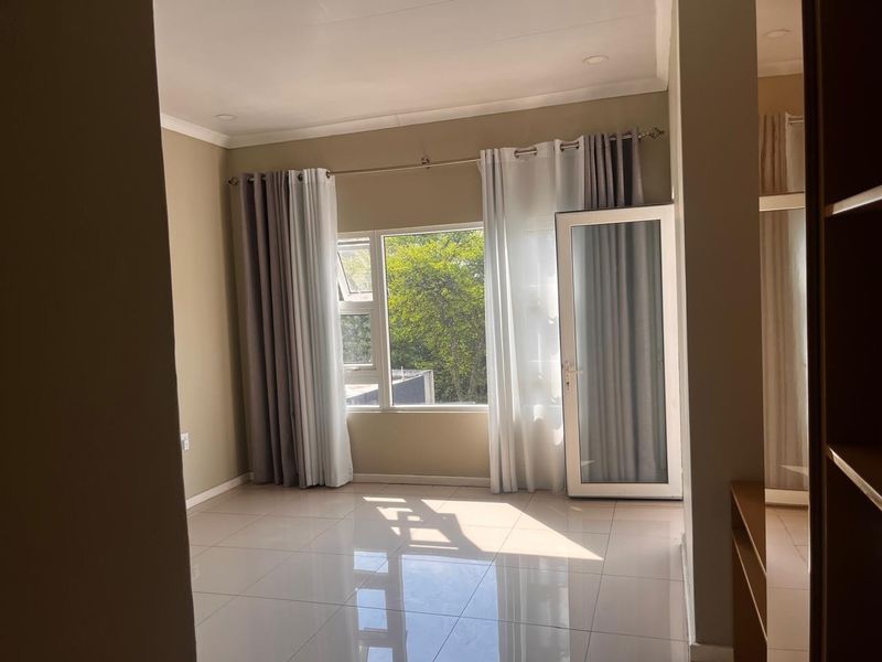 A bright, empty bedroom featuring neutral tiled flooring, modern aluminium window and door frames, and recessed ceiling lighting.