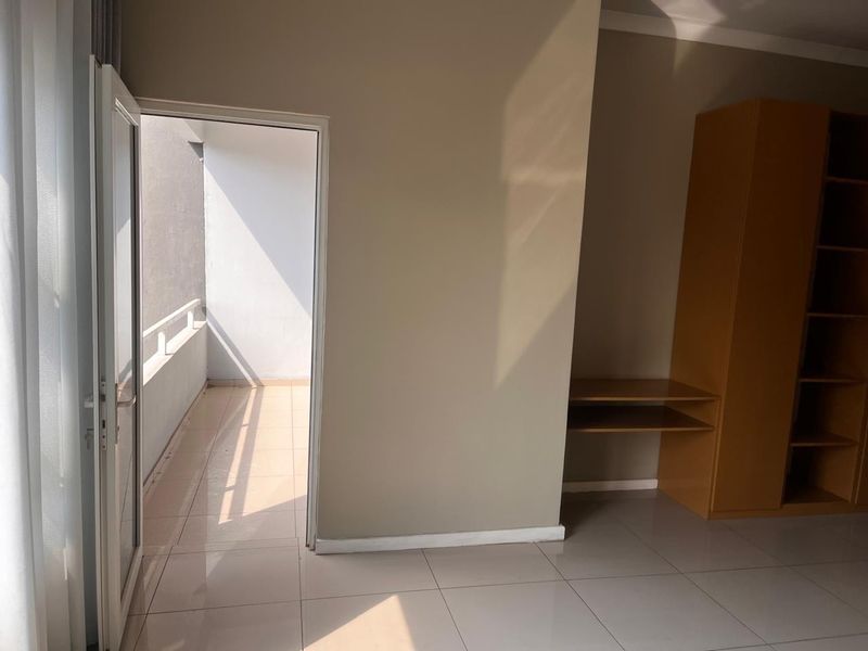 A bright bedroom featuring tiled flooring, a built-in shelving unit, and direct access to an outdoor balcony area.