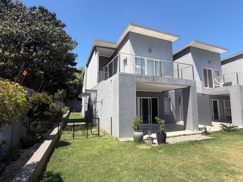 Rear view of a modern apartment building featuring a private balcony, paved patio area, and a small garden space.