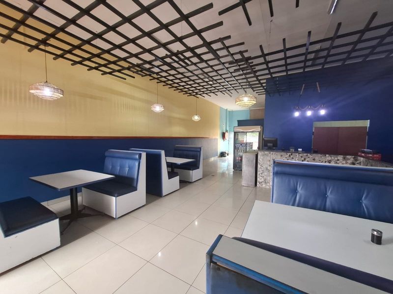 Open plan commercial dining area featuring a suspended grid ceiling, tiled flooring, and a built-in service counter with blue and yellow wall accents.