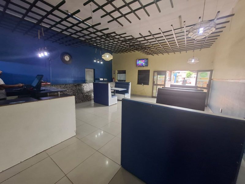 Open-plan commercial dining area featuring fixed booth seating, a service counter, tiled flooring, and a decorative ceiling grid.
