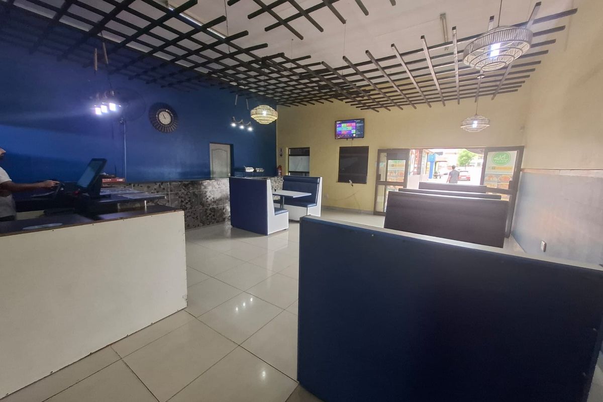 Open-plan commercial dining area featuring fixed booth seating, a service counter, tiled flooring, and a decorative ceiling grid.