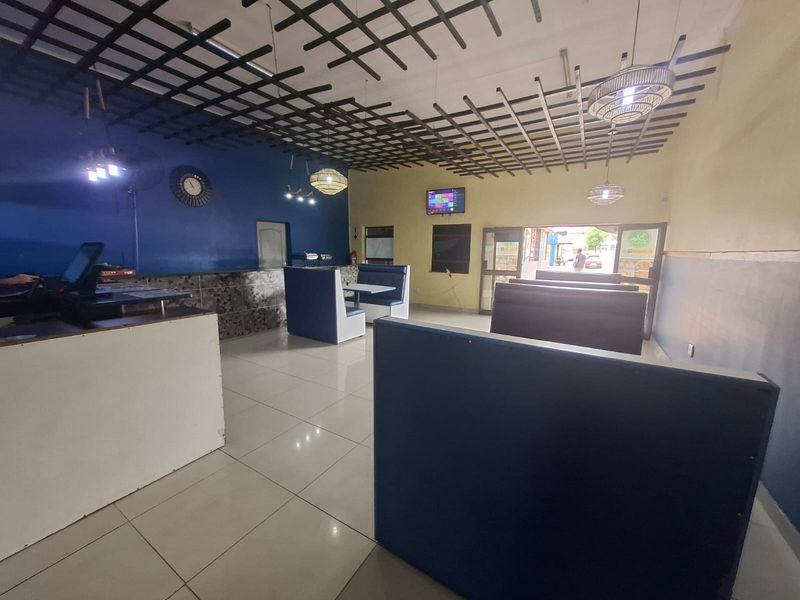 Open plan commercial dining area featuring tiled flooring, a suspended ceiling grid, built-in service counter, and fixed booth seating arrangements.
