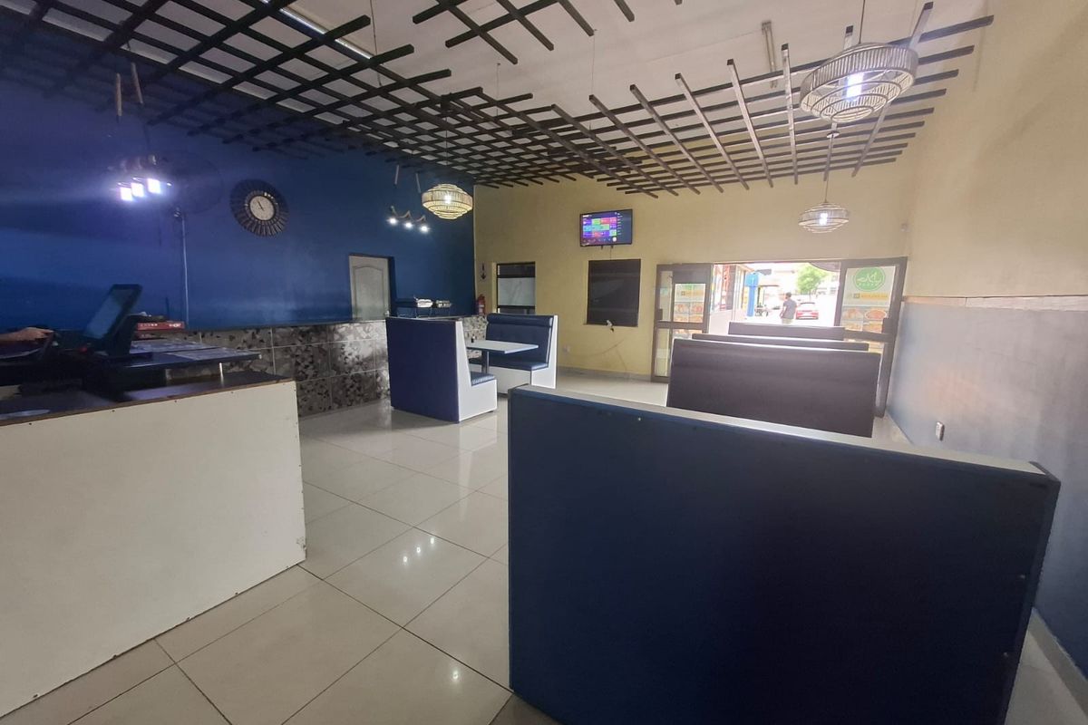 Open plan commercial dining area featuring tiled flooring, a suspended ceiling grid, built-in service counter, and fixed booth seating arrangements.