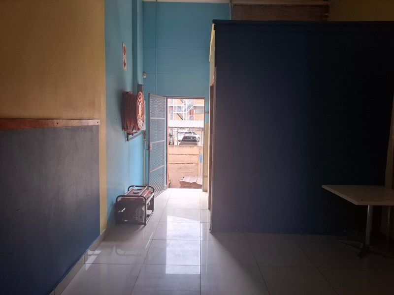 An interior entry area featuring tiled flooring, a wall-mounted fire hose reel, and a security gate leading to an exterior space.