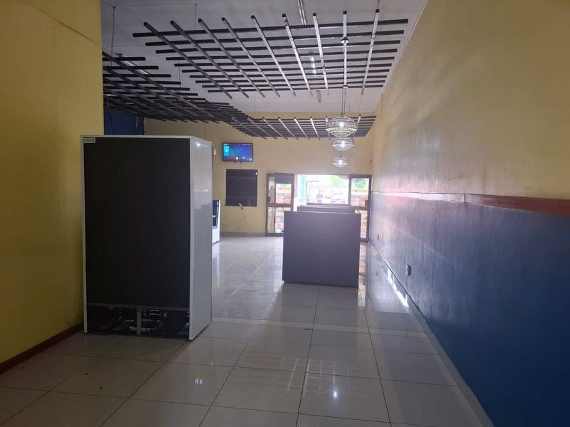 Spacious open-plan commercial unit featuring tiled flooring, a decorative suspended ceiling grid, and large glass entrance doors, suitable for various retail or office uses.