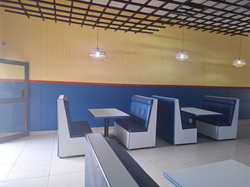 Open plan commercial dining area featuring a suspended ceiling grid, tiled flooring, and built-in booth seating arrangements.