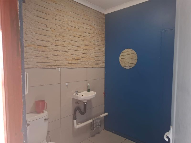 A functional commercial bathroom featuring a wall-mounted basin, toilet, and a decorative stone-clad feature wall.