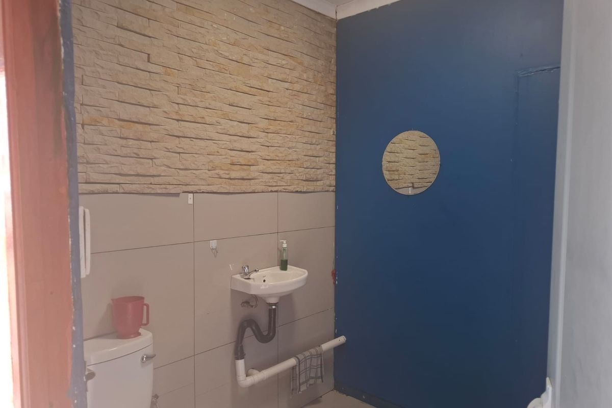 A functional commercial bathroom featuring a wall-mounted basin, toilet, and a decorative stone-clad feature wall.