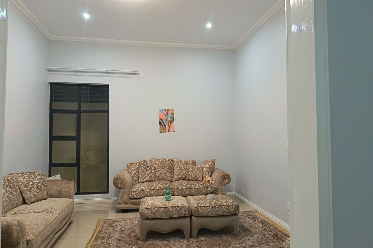 A well-maintained living room featuring neutral tiled flooring, recessed downlighting, and a large aluminium-framed window, offering a clean and bright living space.