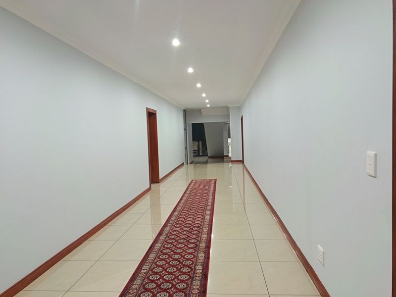 A spacious, well-lit hallway featuring neutral walls, polished tile flooring, and clean architectural lines leading to the interior living spaces.