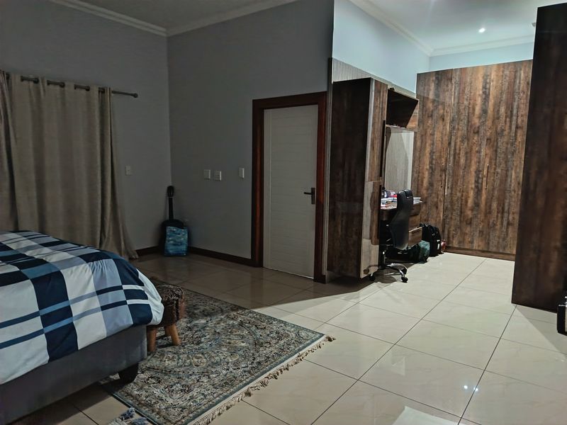 Spacious bedroom featuring large built-in wooden cupboards, a dedicated built-in desk area, and neutral tiled flooring throughout.