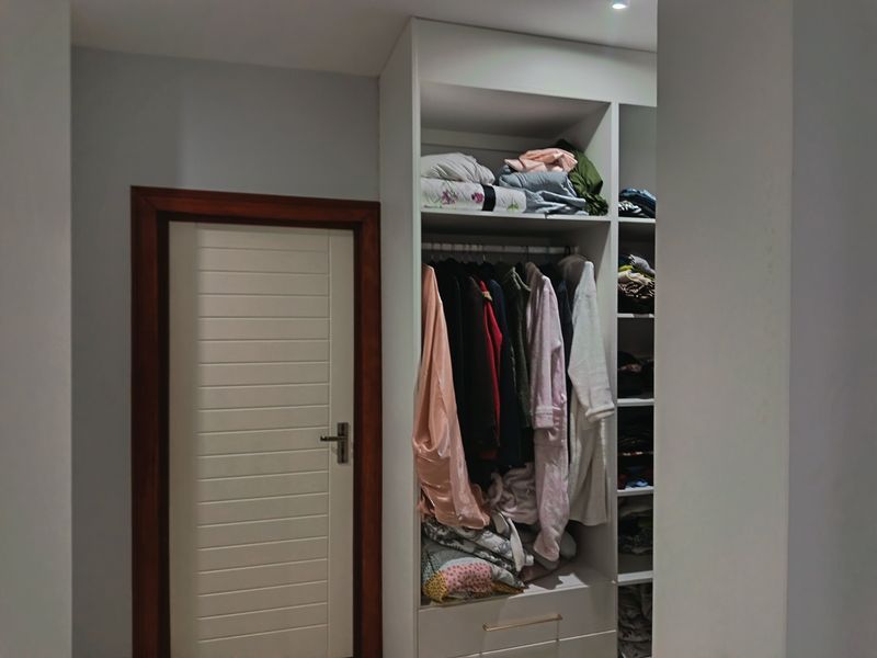 A bedroom featuring a built-in wardrobe with open shelving and hanging space, complemented by a solid internal door with a wooden frame.