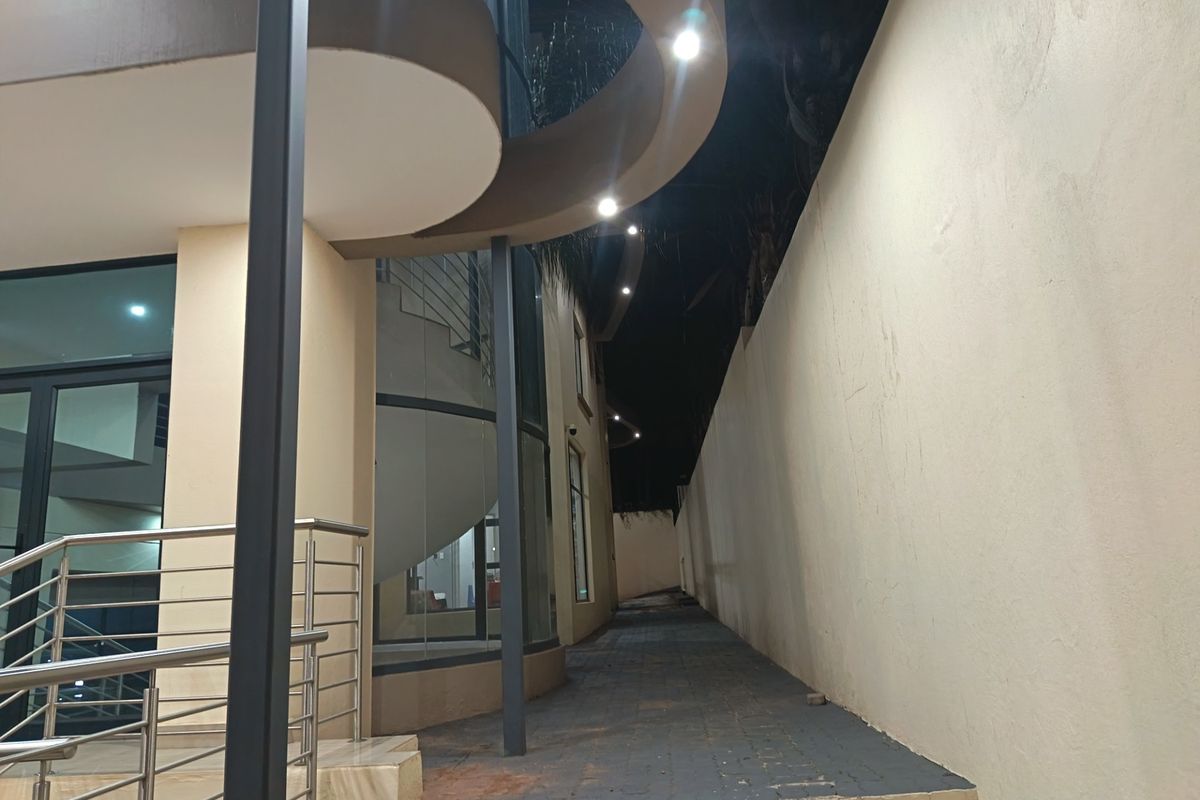 Night view of the rear exterior featuring a modern curved facade, glass architectural elements, a spiral staircase, and a paved walkway along a retaining wall.