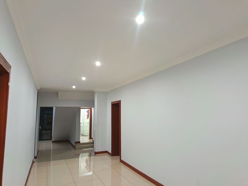 A spacious, well-lit hallway featuring neutral walls, tiled flooring, and recessed downlighting, providing a clean and open transition between rooms.