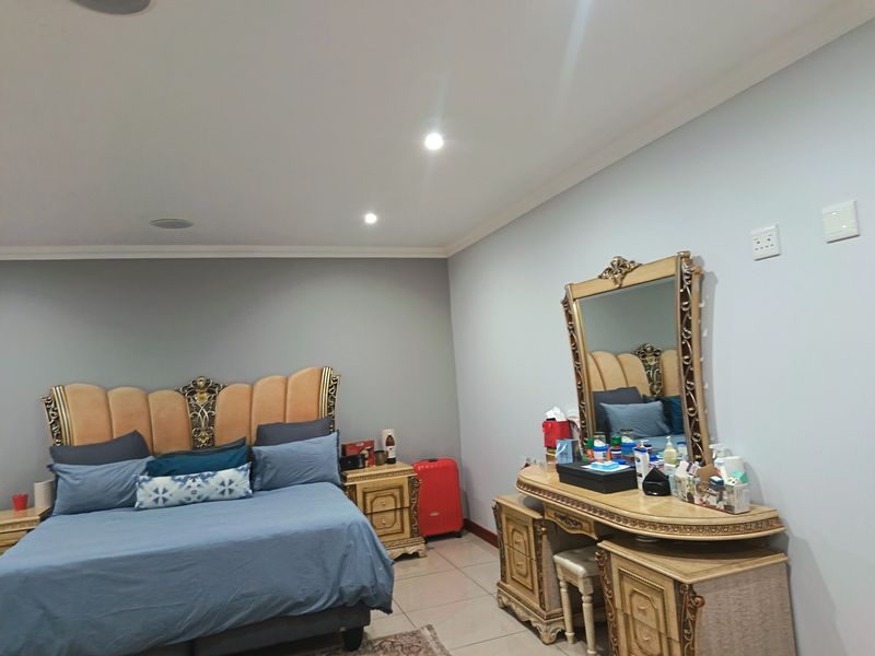 A spacious bedroom featuring tiled flooring, recessed ceiling lighting, and integrated ceiling speakers, providing a comfortable and functional living space.