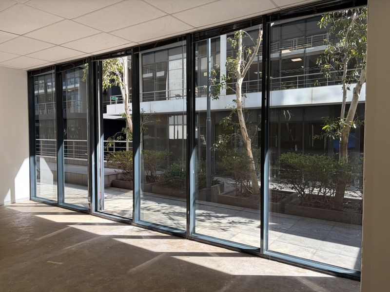 A bright, empty office space featuring large floor-to-ceiling windows that provide ample natural light and views of the exterior courtyard.
