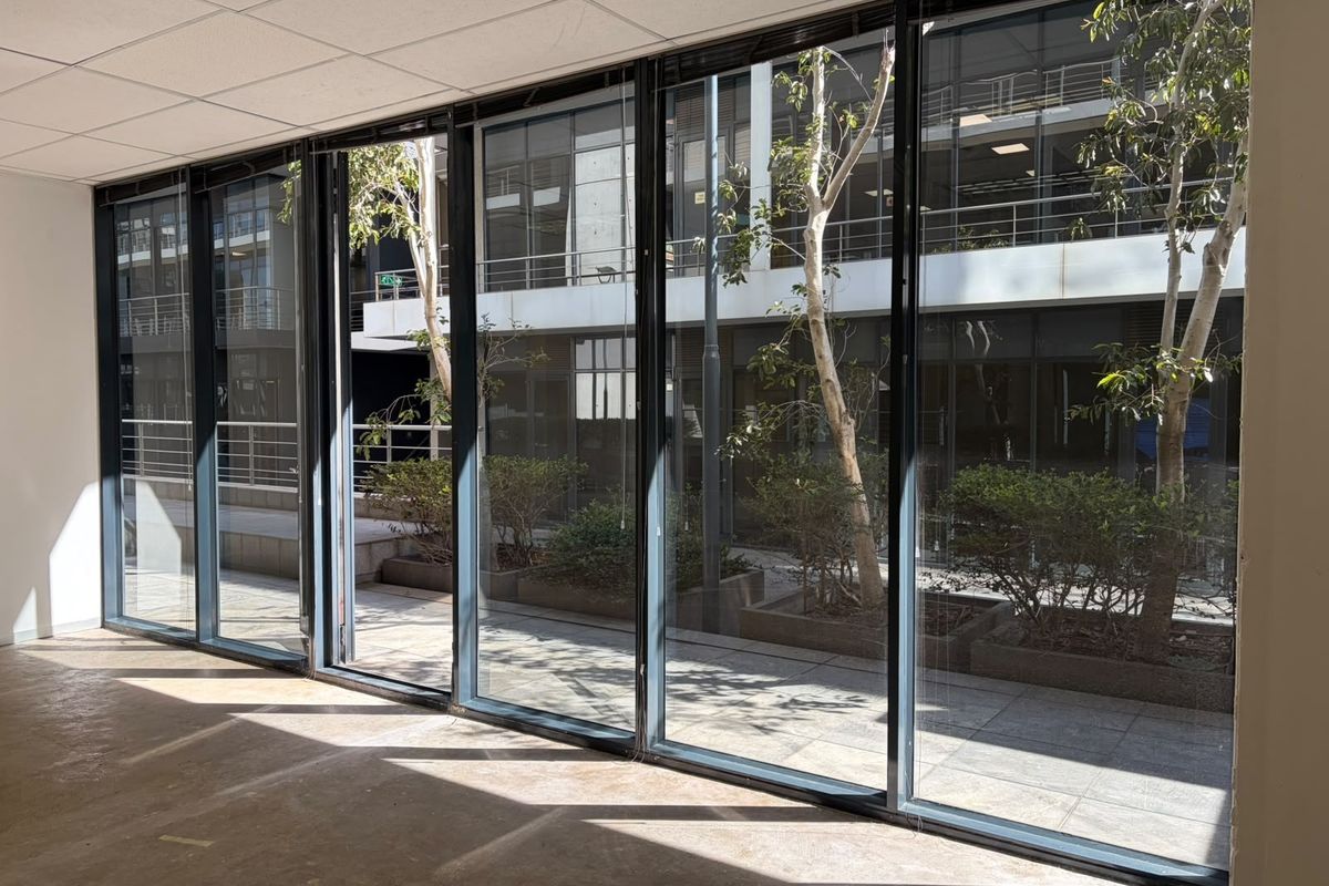 A bright, empty office space featuring large floor-to-ceiling windows that provide ample natural light and views of the exterior courtyard.