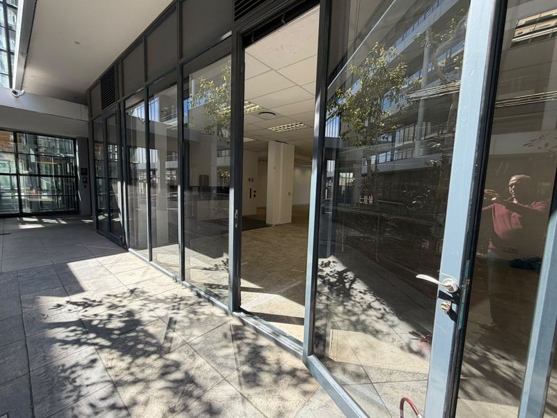 A modern office space with extensive glass frontage, tiled flooring, and a suspended ceiling, offering a bright and professional environment.