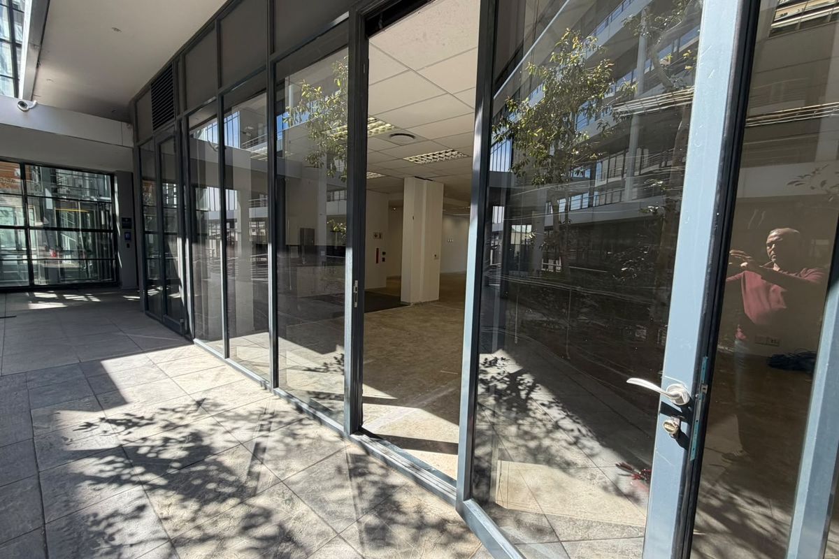 A modern office space with extensive glass frontage, tiled flooring, and a suspended ceiling, offering a bright and professional environment.
