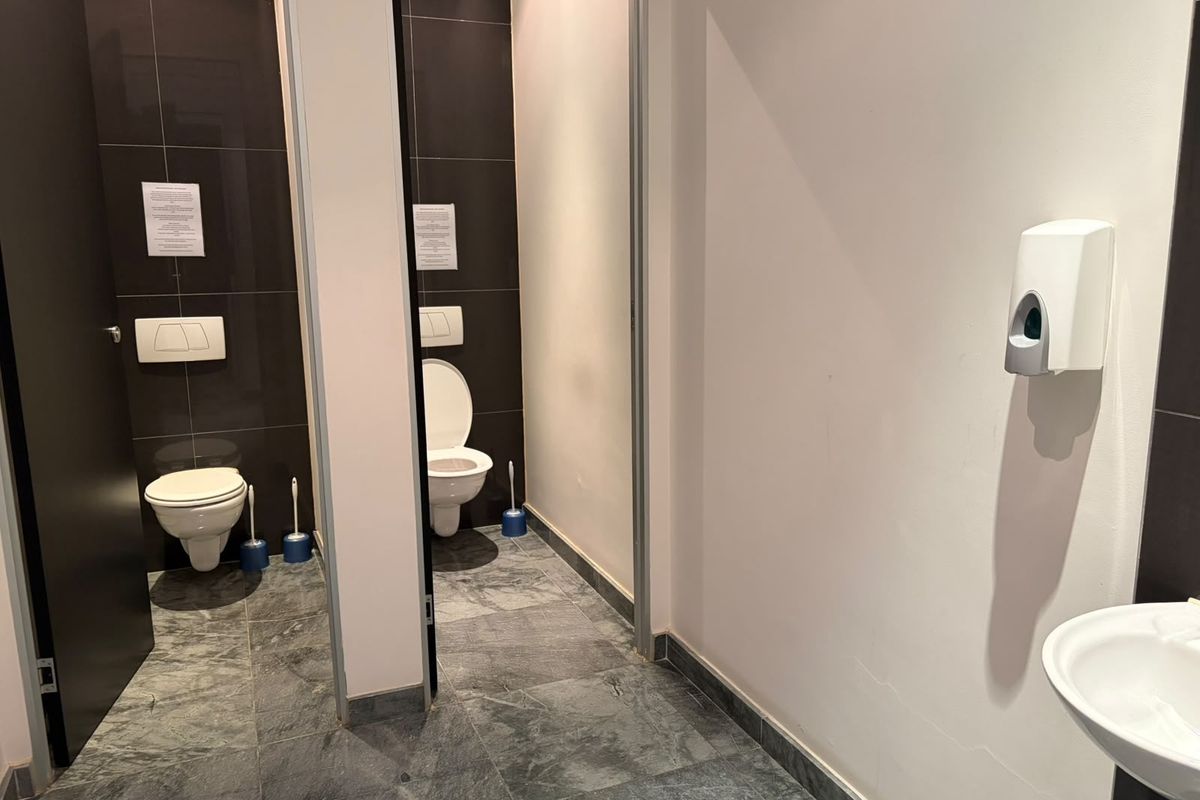 A clean, modern office restroom featuring two private toilet stalls with wall-mounted fixtures and a shared washbasin area with tiled finishes.